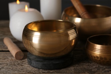 Photo of Golden singing bowls, mallets and burning candles on wooden table, closeup
