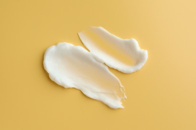 Photo of Samples of face cream on yellow background, top view