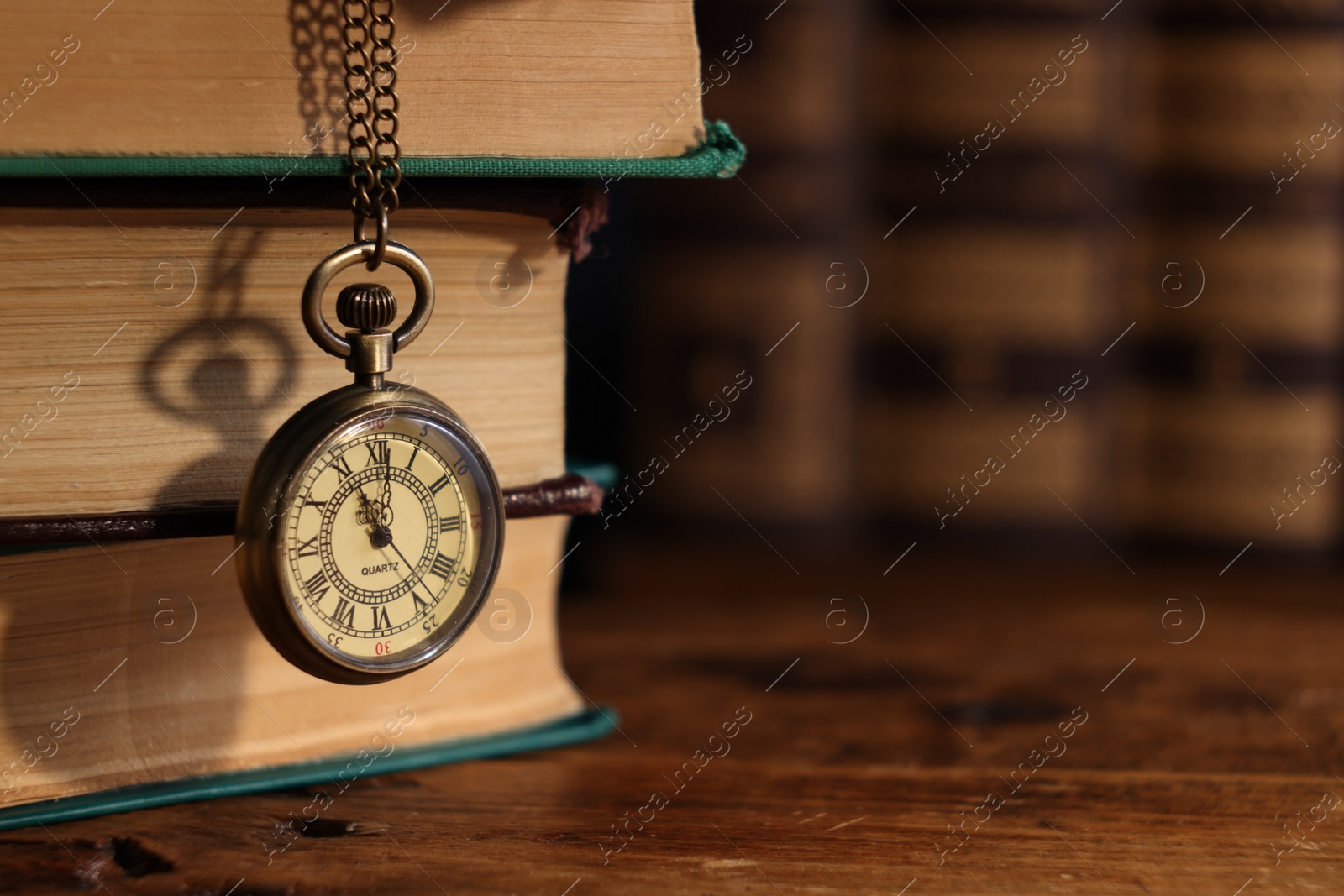 Photo of Pocket clock hanging on stack of books at wooden table, closeup. Space for text