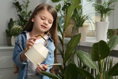 Cute little girl watering beautiful green plant at home. House decor