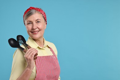 Happy housewife with spoons on light blue background, space for text