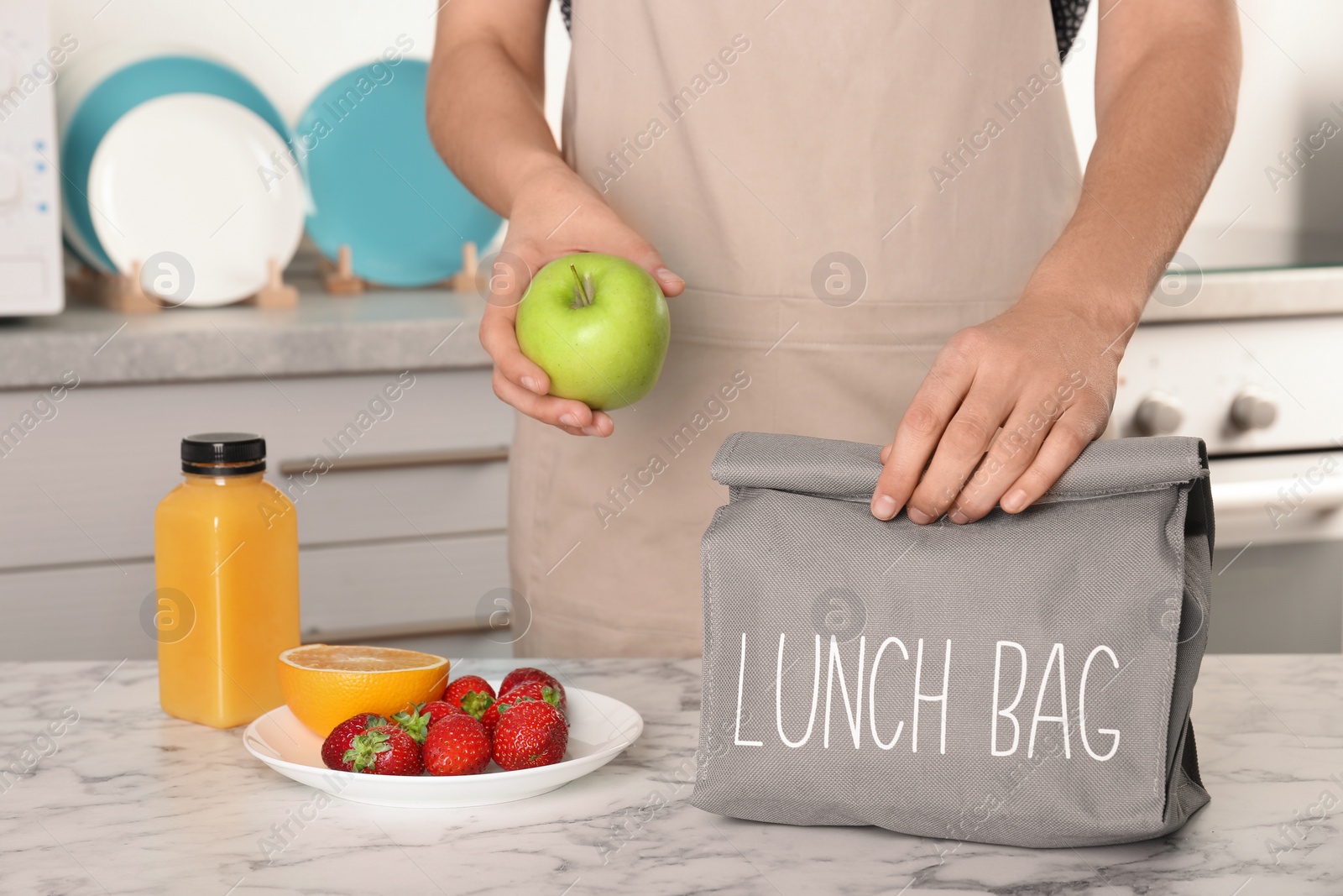 Photo of Woman packing food for her child at table in kitchen, closeup. Healthy school lunch