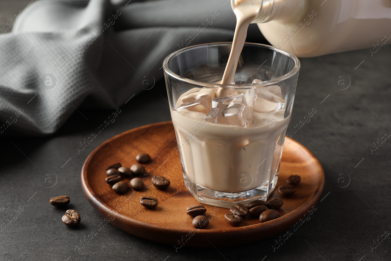 Photo of Pouring coffee cream liqueur into glass at grey table, closeup