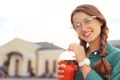 Young woman with refreshing drink on city street. Space for text