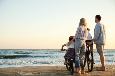 Family with bicycles on sandy beach near sea