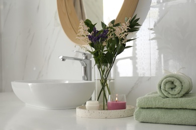 Photo of Beautiful flowers, towels and candle on countertop in bathroom. Interior decor