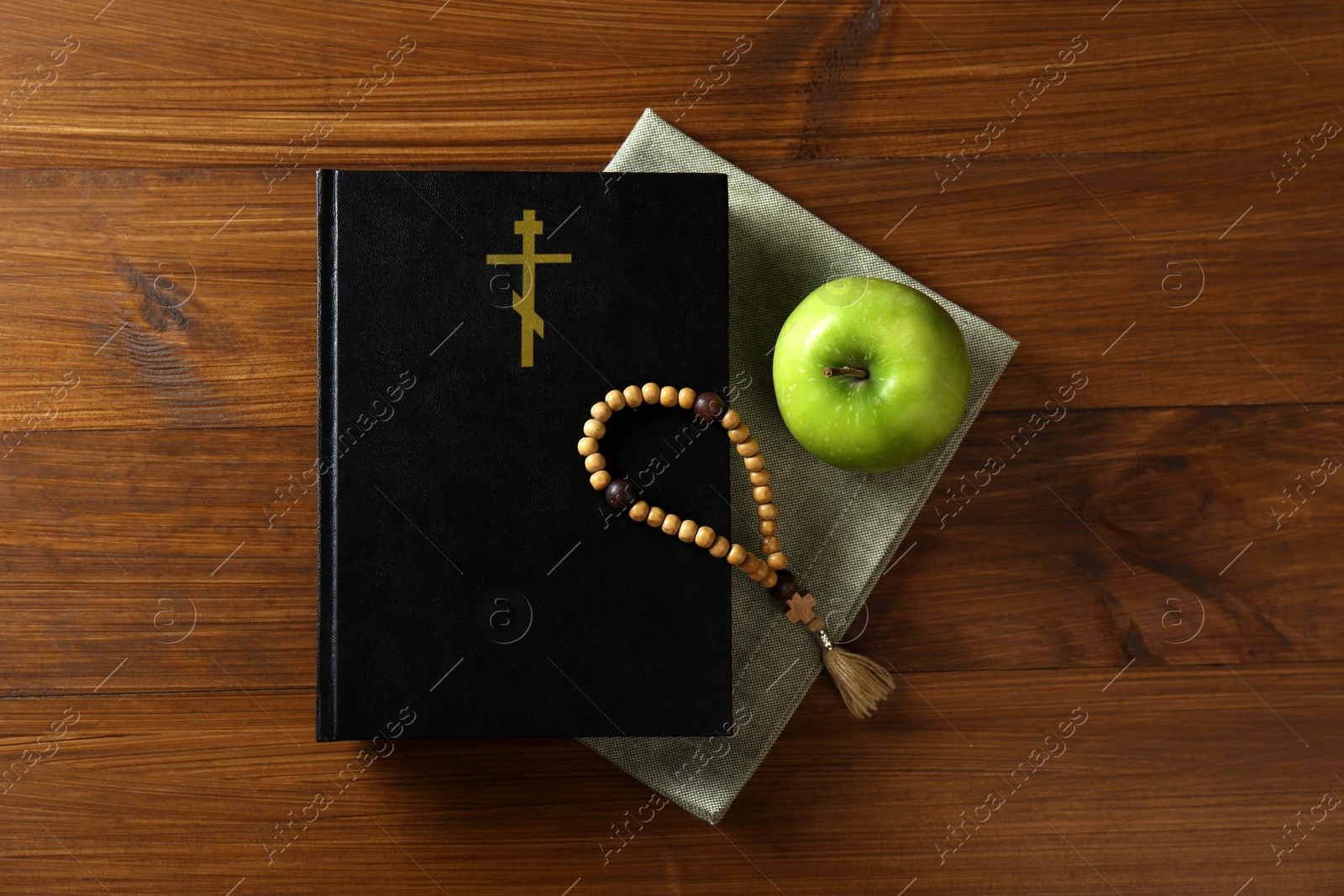 Photo of Bible, rosary beads and apple on wooden table, flat lay. Lent season