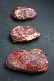 Pieces of raw beef meat on dark grey textured table, flat lay