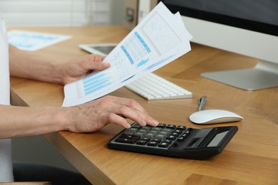 Professional accountant using calculator at wooden desk in office, closeup