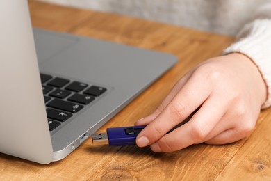 Woman attaching usb flash drive into laptop at wooden table, closeup