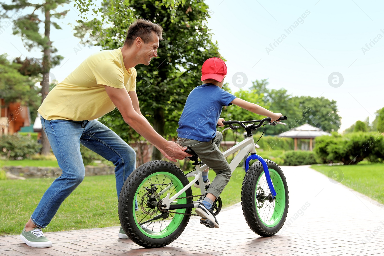 Photo of Dad teaching son to ride bicycle outdoors