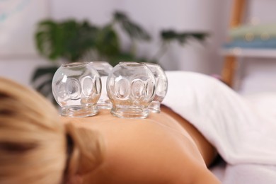 Cupping therapy. Closeup view of woman with glass cups on her back indoors, space for text