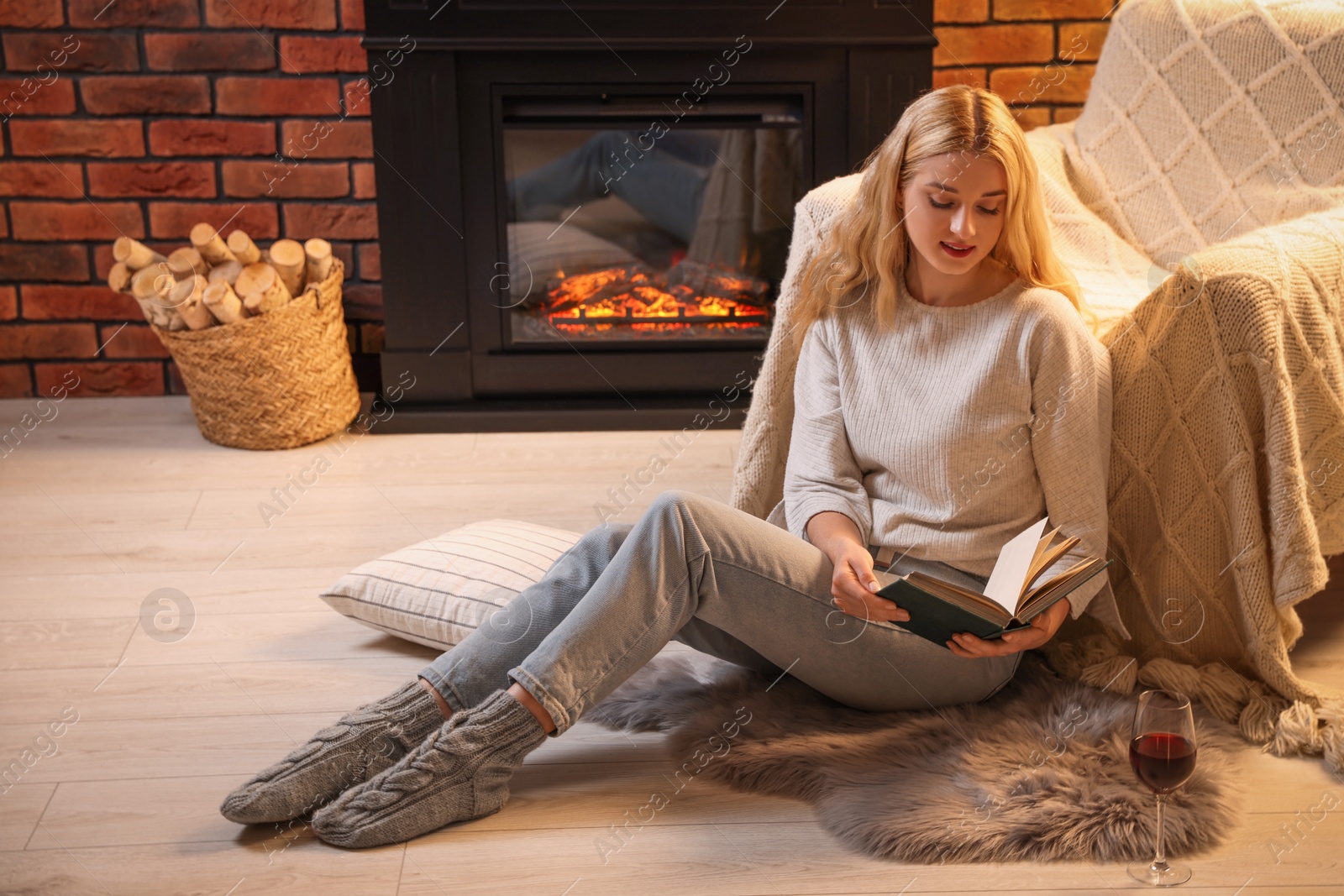 Photo of Beautiful young woman reading book near fireplace in room