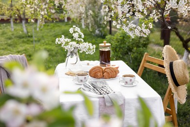 Photo of Stylish table setting with beautiful spring flowers, tea and croissants in garden