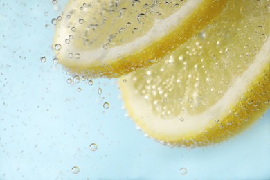 Juicy lemon slices in soda water against light blue background, closeup