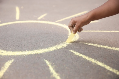 Photo of Little child drawing sun with chalk on asphalt