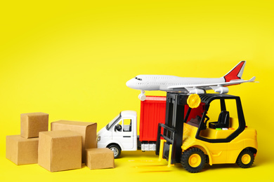 Photo of Different toy vehicles with boxes on yellow background. Logistics and wholesale concept