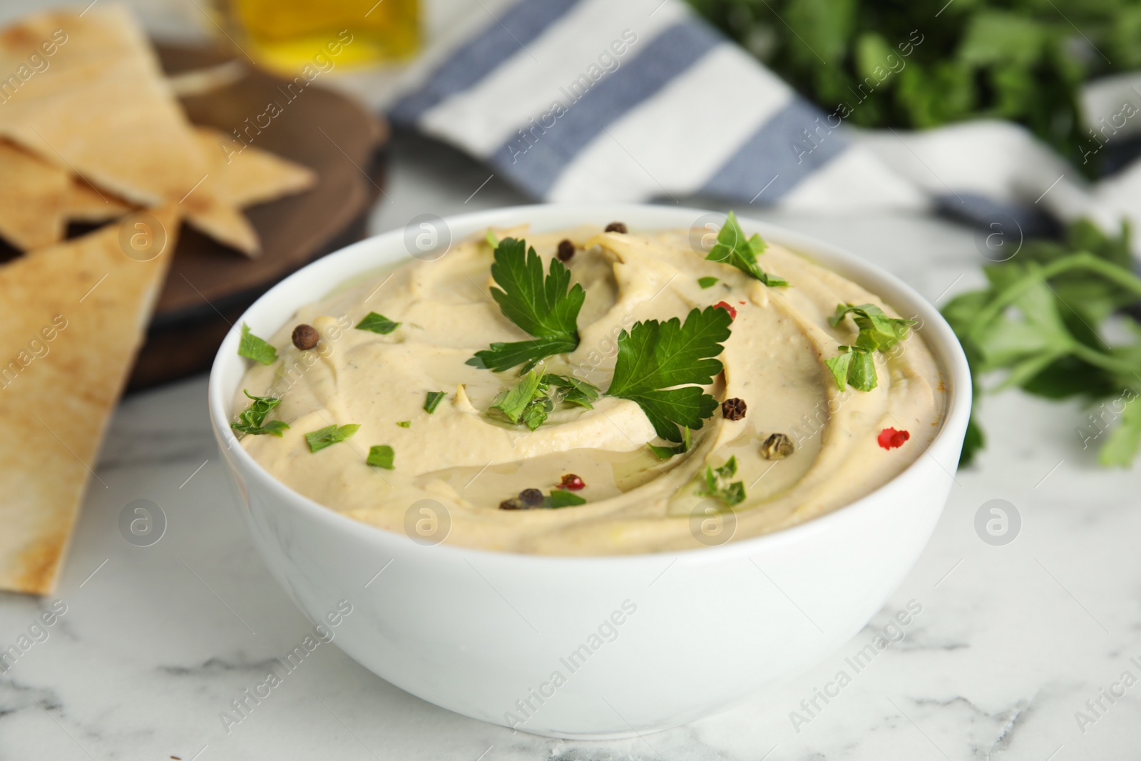 Photo of Delicious hummus with parsley and pita chips on white marble table, closeup