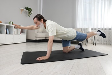 Senior man in sportswear doing exercises on fitness mat at home