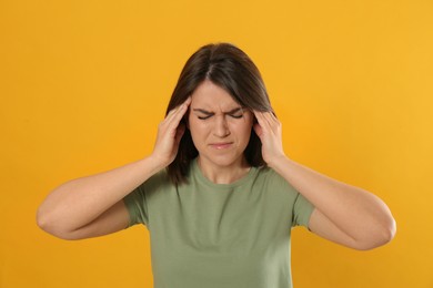 Photo of Young woman suffering from migraine on yellow background