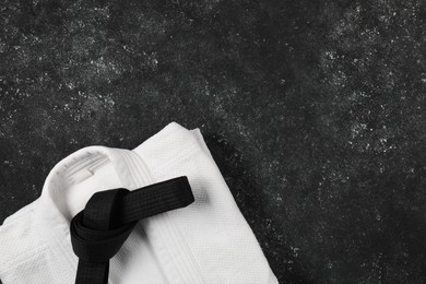 Black karate belt and white kimono on gray textured background, top view. Space for text