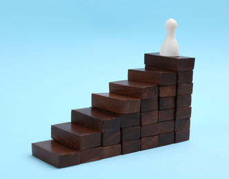 Photo of White piece on top of wooden stairs against light blue background. Career promotion concept