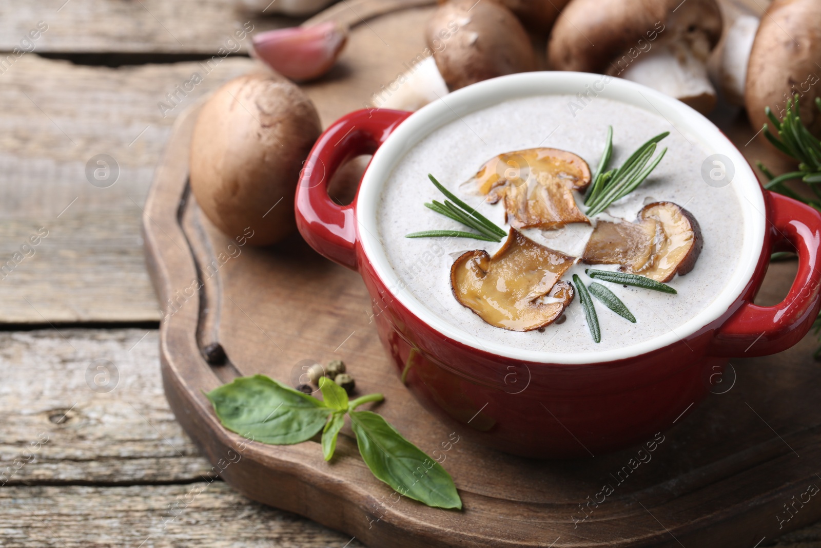 Photo of Delicious homemade mushroom soup in ceramic pot and fresh ingredients on wooden table. Space for text