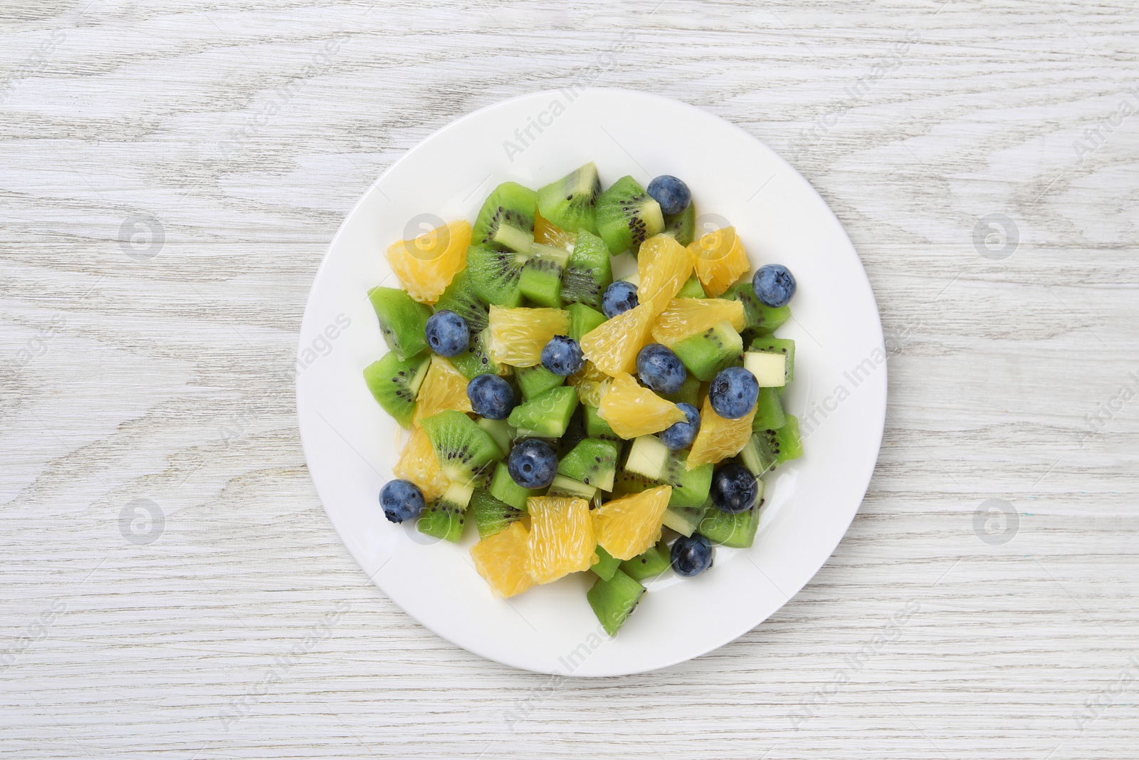 Photo of Plate of tasty fruit salad on white wooden table, top view