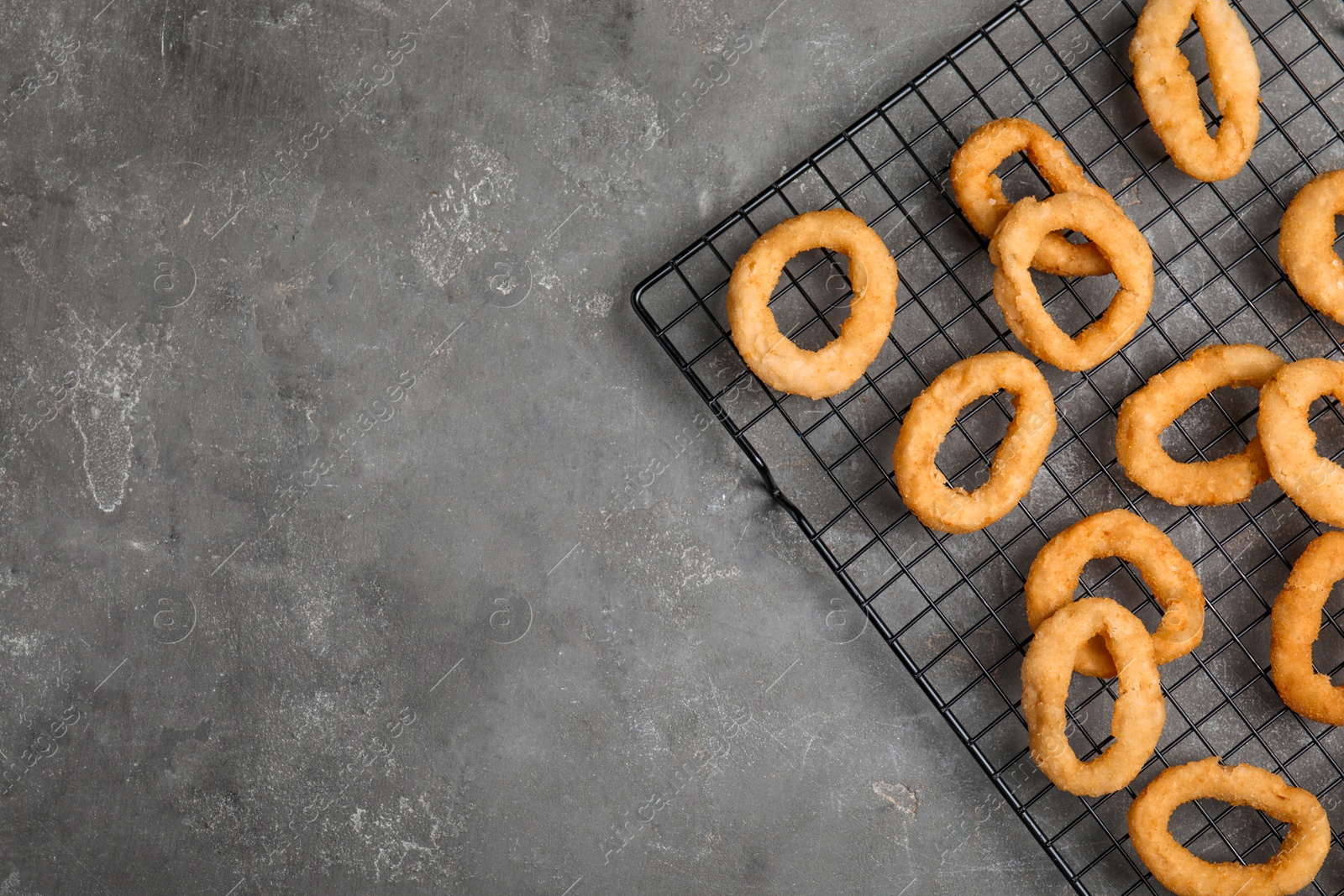 Photo of Cooling rack with fried onion rings on grey table, top view. Space for text