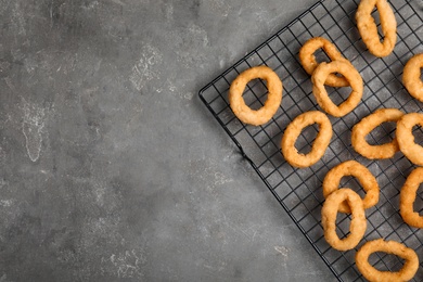 Photo of Cooling rack with fried onion rings on grey table, top view. Space for text