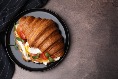 Tasty croissant with fried egg, tomato and microgreens on brown textured table, top view. Space for text