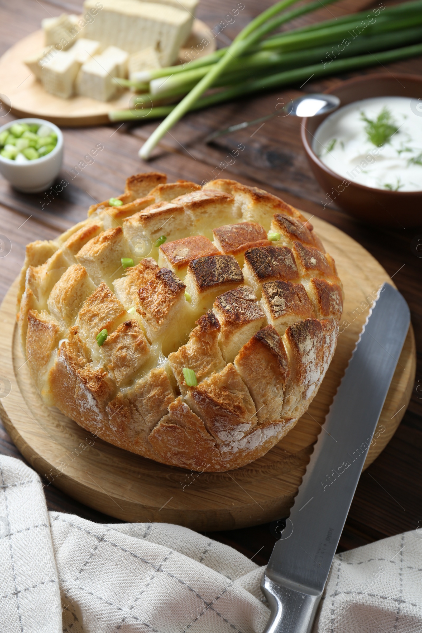 Freshly baked bread with tofu cheese, green onions, sauce and knife on wooden table Photo of Freshly baked bread with tofu cheese, green onions, sauce and knife on wooden table