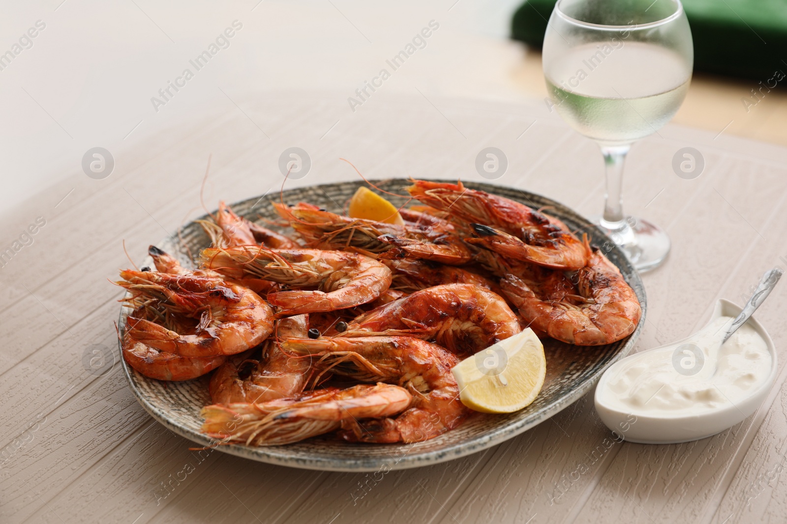 Photo of Plate of delicious cooked shrimps served with lemon, sauce and wine at table