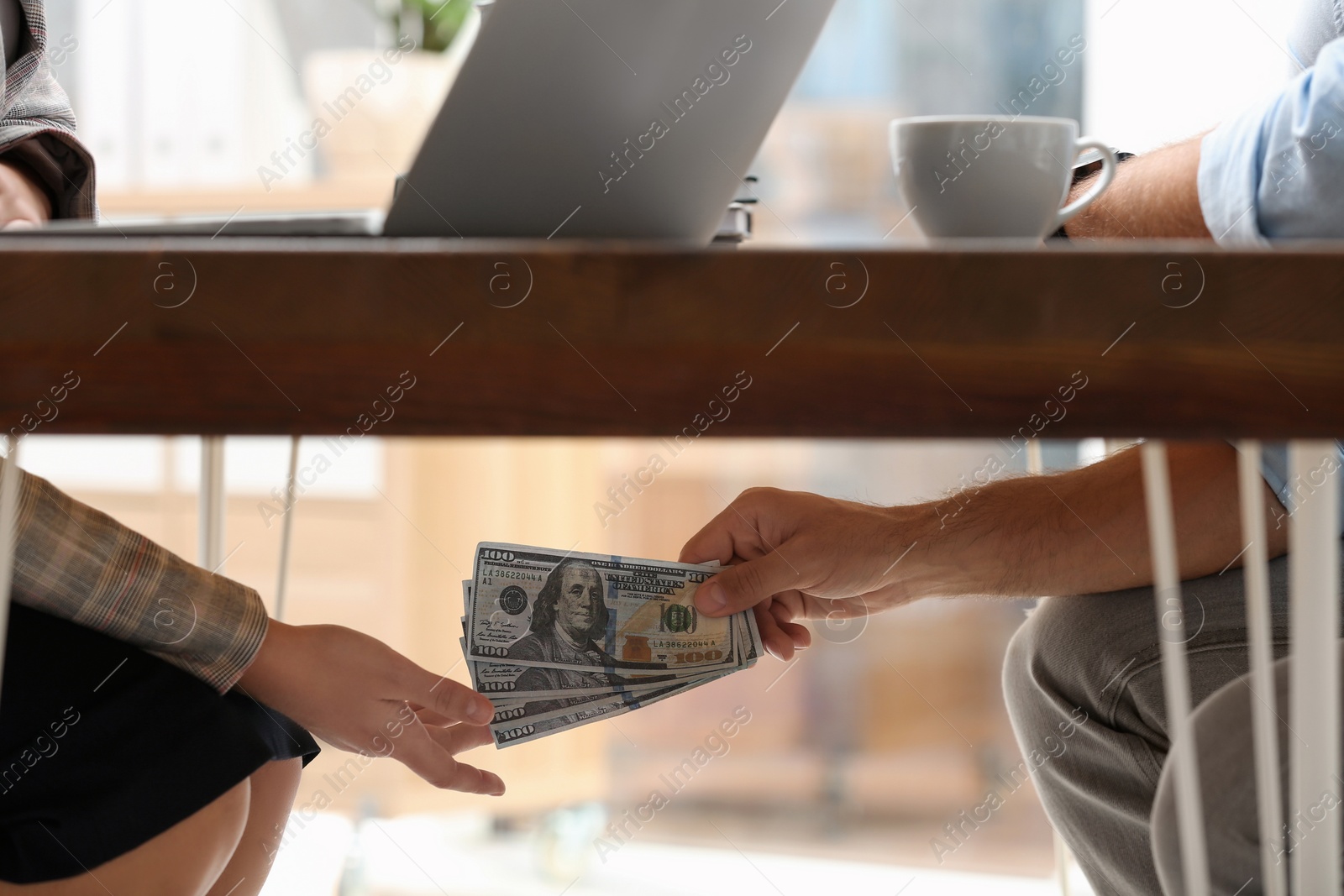 Photo of Man giving bribe money to woman under table in office, closeup