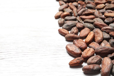 Photo of Tasty cocoa beans on white wooden table, space for text