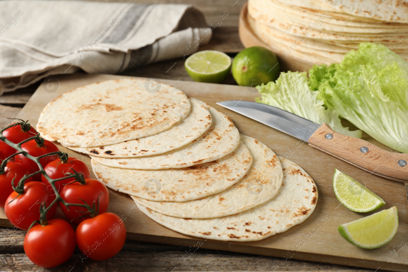 Photo of Tasty homemade tortillas, tomatoes, lime, lettuce and knife on wooden table