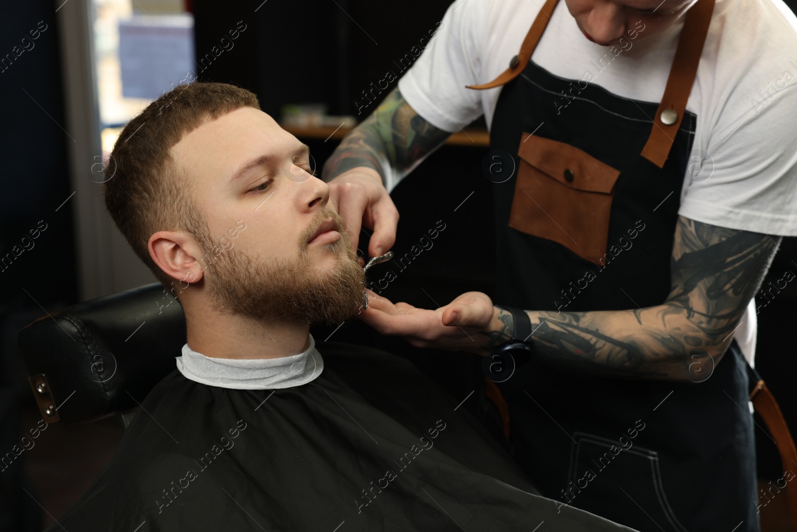 Photo of Professional hairdresser working with bearded client in barbershop