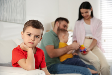 Unhappy little boy feeling jealous while parents spending time with his baby brother at home