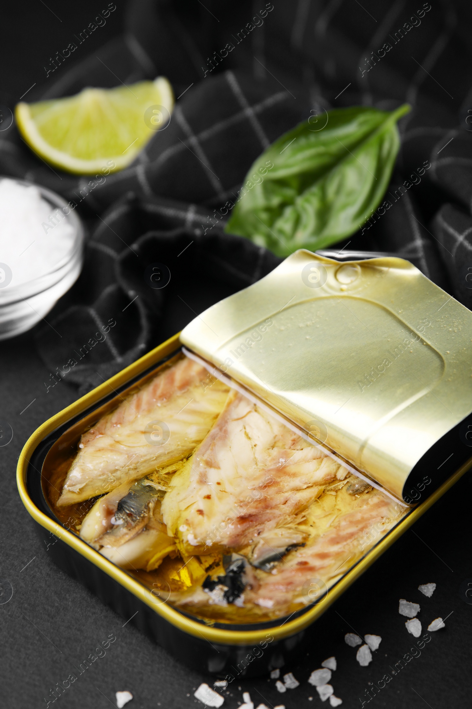Photo of Open tin can with mackerel fillets on black table, closeup
