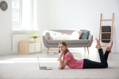 Teenage girl with laptop lying on cozy carpet at home