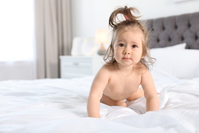 Adorable little baby girl crawling on bed in room. Space for text