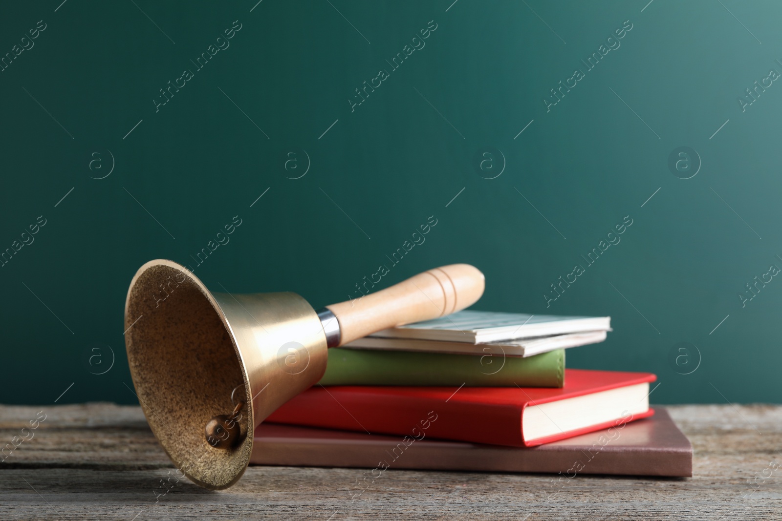 Photo of Golden bell and books on wooden table near green chalkboard. School days