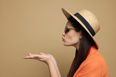 Photo of Beautiful young woman in straw hat blowing kiss on beige background. Space for text