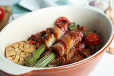 Photo of Oven baked asparagus wrapped with bacon in ceramic dish on white table, closeup