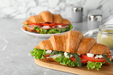 Photo of Tasty croissant sandwich with feta cheese and tomato on light grey marble table