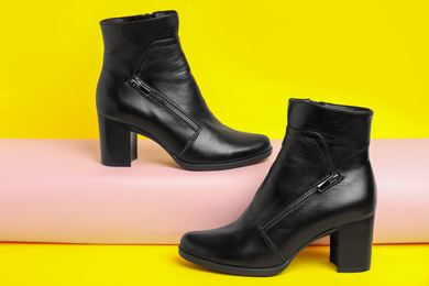 Stylish black female boots on yellow background