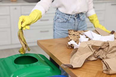 Photo of Garbage sorting. Woman throwing banana peel into trash bin indoors, closeup