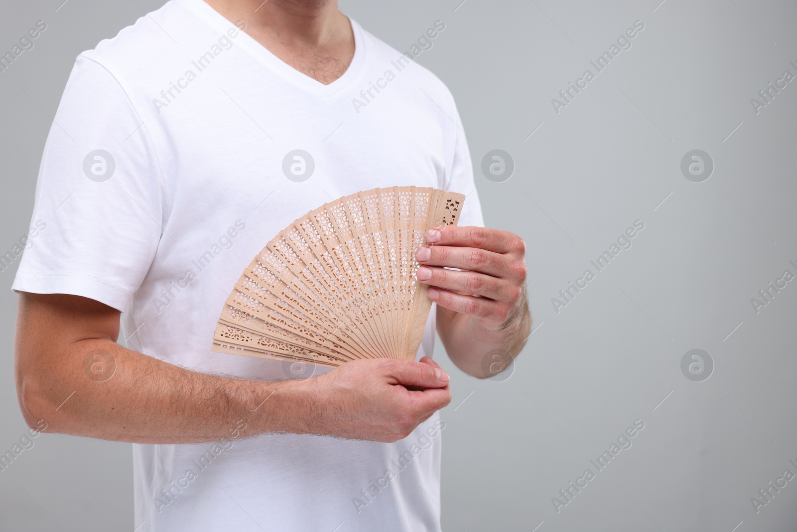 Photo of Man holding hand fan on light grey background, closeup. Space for text