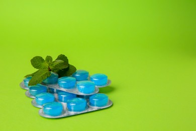 Photo of Blisters with cough drops and mint leaves on light green background. Space for text