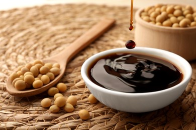 Photo of Soy sauce drops falling into bowl on wicker mat, closeup